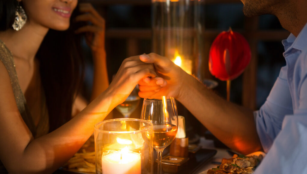 Romantic couple holding hands together over candlelight during romantic dinner